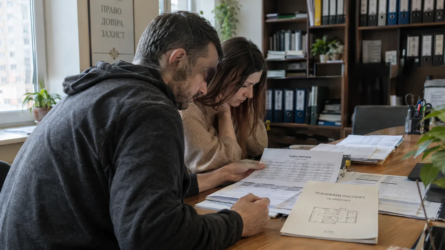 Покупець і продавець сидять за довгим столом у приймальні нотаріальної контори, перед ними розкладені графік платежів і технічний паспорт