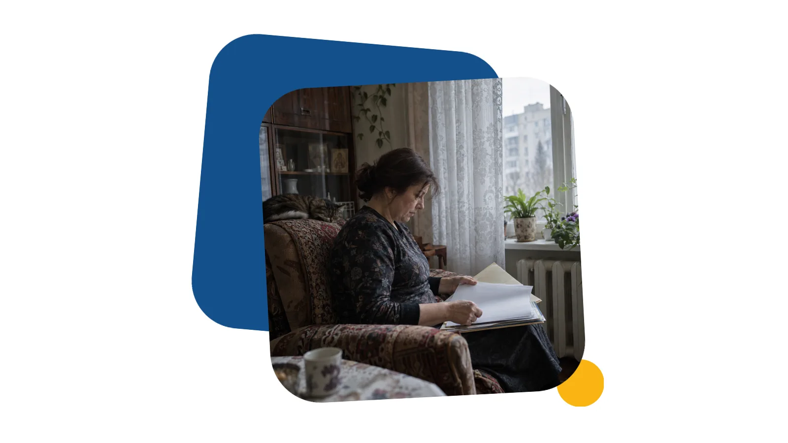 Жінка середнього віку сидить біля вікна в старій квартирі й переглядає теку з паперами, видно її збоку