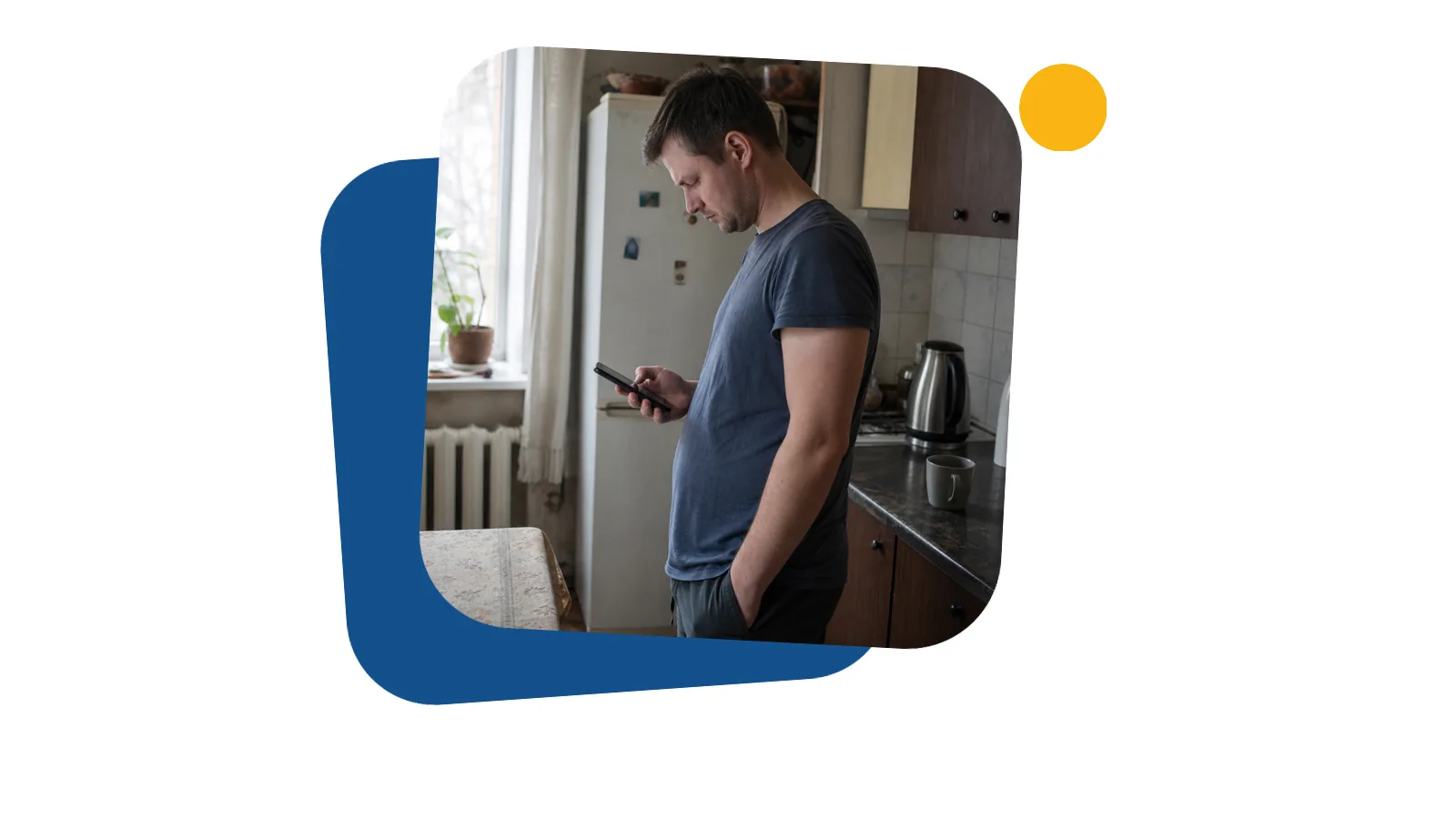 Мужчина на кухне арендованной квартиры читает сообщение на телефоне и хмурится