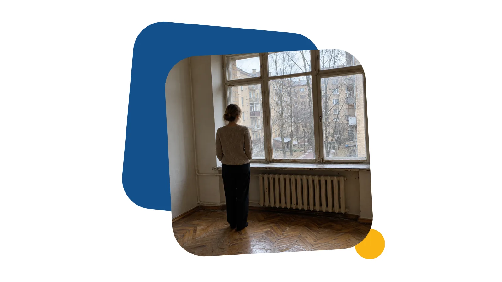 Женщина со спины стоит в пустой светлой комнате квартиры в старом доме и смотрит в окно на двор