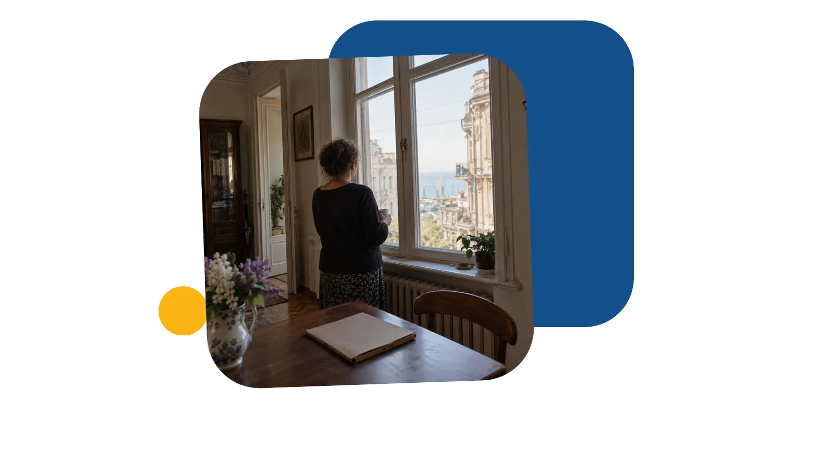 Жінка стоїть спиною біля вікна в старій одеській квартирі з високими стелями, на столі поруч тека з документами
