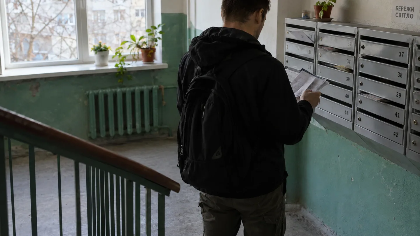 Чоловік зі спини переглядає папери на столі в коридорі багатоквартирного будинку